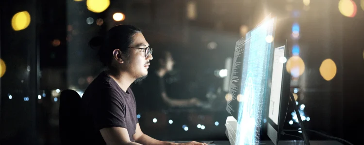 man with glasses looking at 3 large monitors