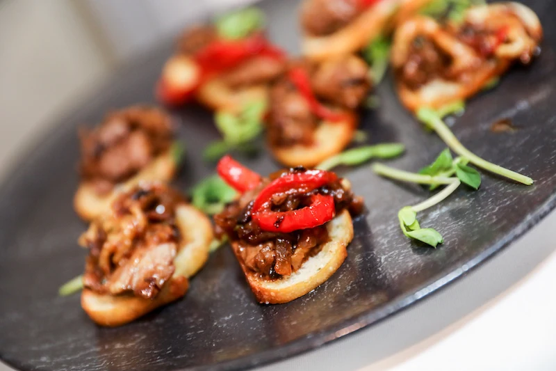 Close up shot of a plate filled with individual bite sized appetizers, duck breast on a crostini