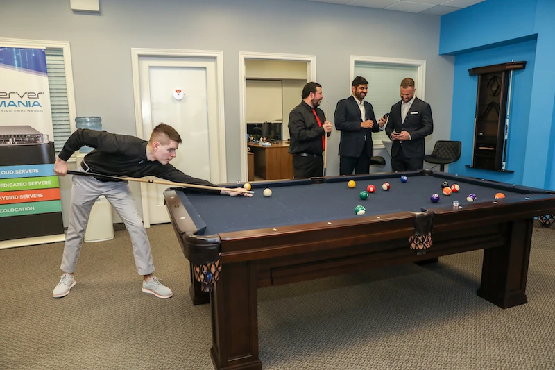 Employees gathered around a pool table as one employee takes a shot